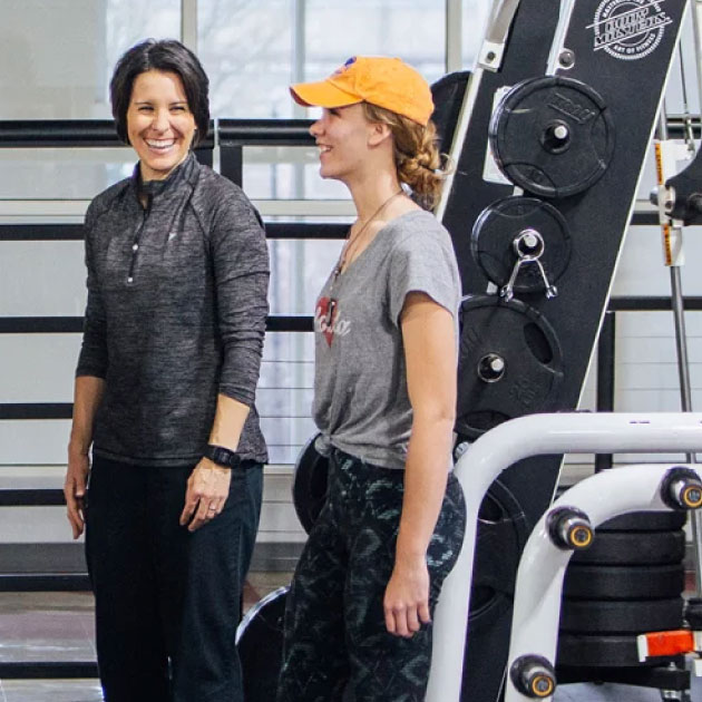 A professor and student stand among exercise equipment in an indoor gym